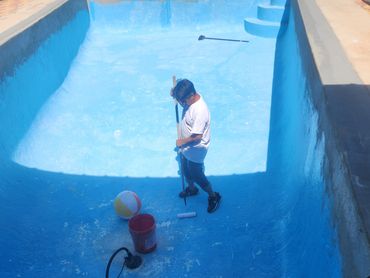 Man cleaning and painting an empty pool with a roller.