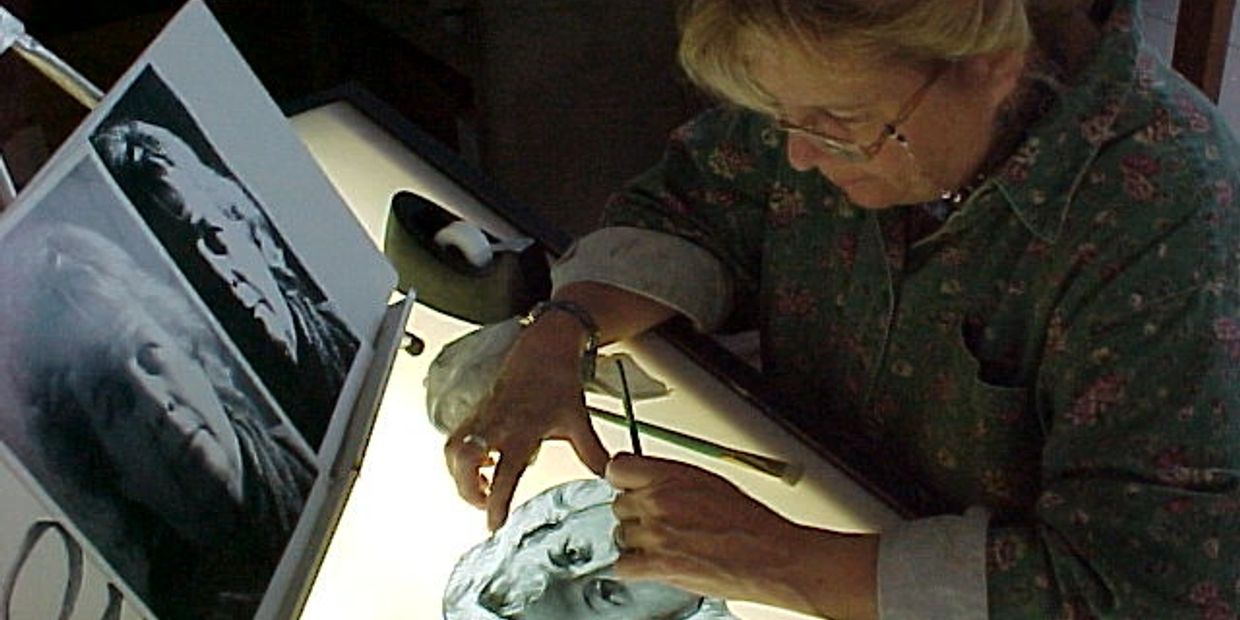 An artist sculpts a detailed bust using photo references.