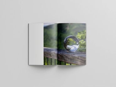Open book showing a photo of a glass sphere on a wooden railing with greenery reflected inside.