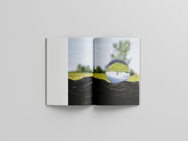 Open book with a photo of a glass orb reflecting an inverted landscape.