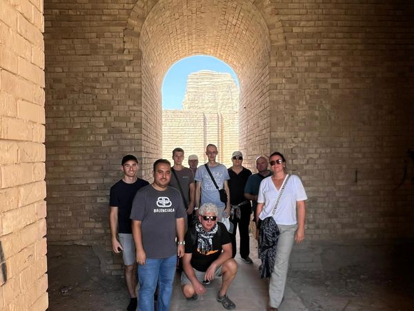 Group of tourists posing inside an ancient brick archway at a historic site.