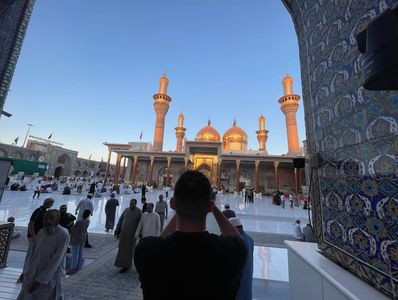 Golden-domed mosque with people gathered in the courtyard at sunset.