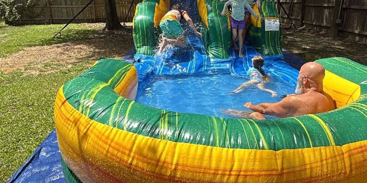 Children and an adult enjoying an inflatable water slide in a backyard.