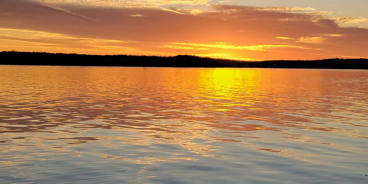 Sunset over calm water with boat railing in view.