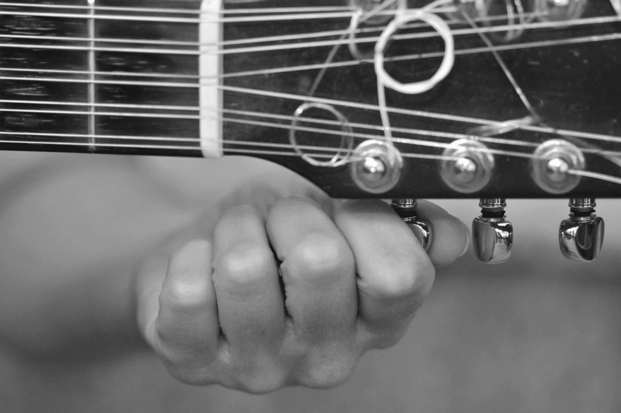 Close-up of a hand tuning guitar strings on the headstock.