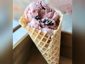 Scoops of pink ice cream in a waffle cone with chocolate chunks.