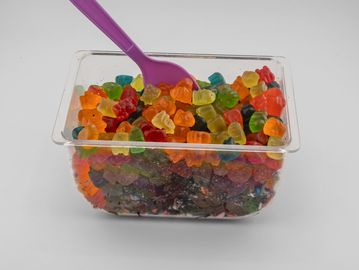 Container filled with colorful gummy bears and a purple spoon.