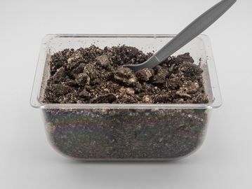 Plastic container filled with crushed chocolate cookies and a gray spoon.