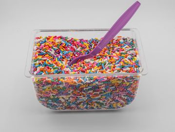 Plastic container filled with colorful candy sprinkles and a purple plastic spoon.