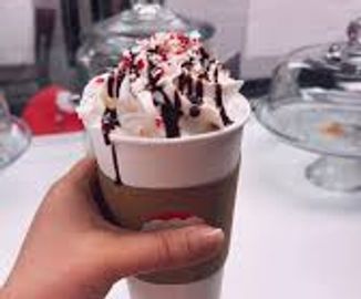 Hand holding a cup of iced coffee topped with whipped cream and chocolate drizzle.