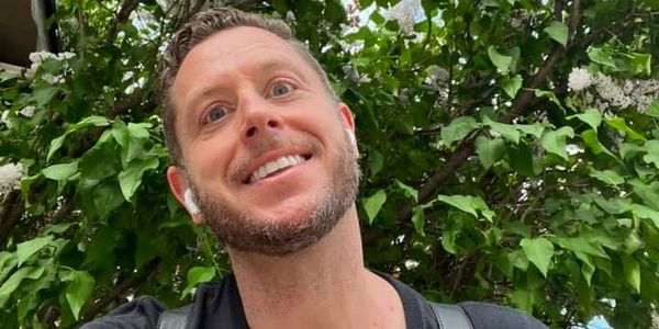 Man smiling outdoors with blooming white lilac flowers behind.