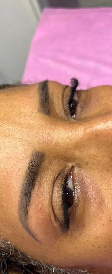 Close-up of freshly done eyelash extensions and shaped eyebrows on a person lying down.