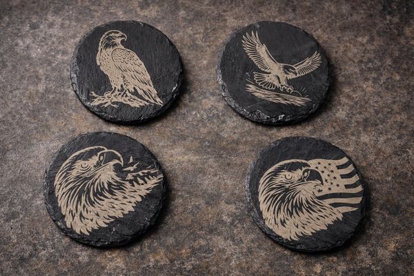 Four round black coasters with detailed eagle engravings.