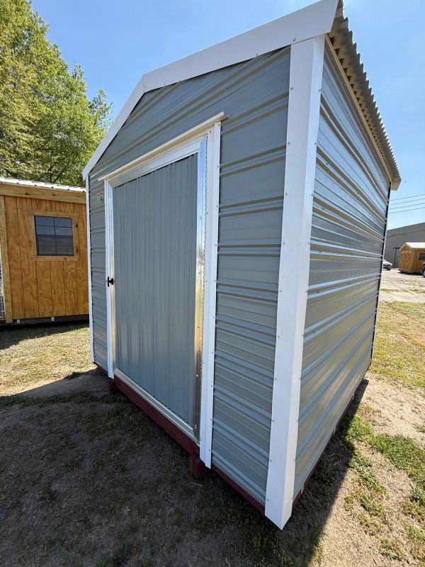 Small metal storage shed with a sliding door under a clear sky.