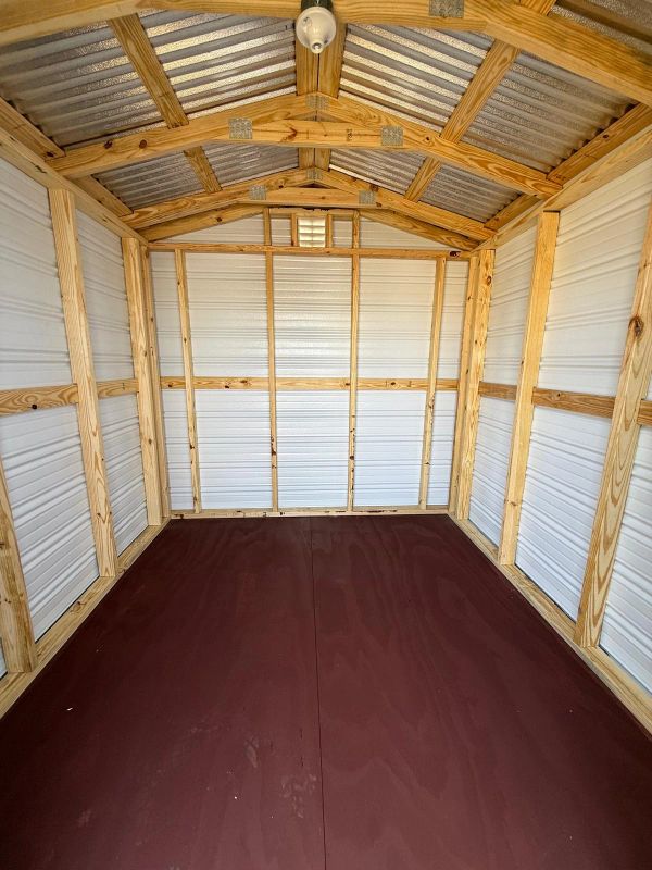 Empty wooden and metal storage shed with a brown floor.