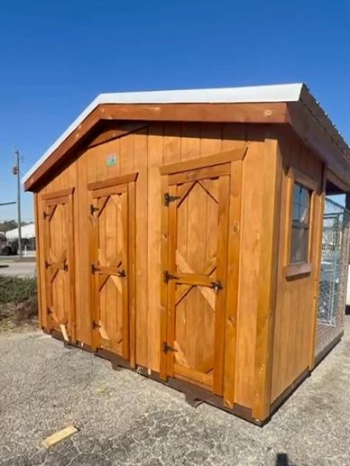 Wooden outdoor shed with three doors and a small window on a sunny day.