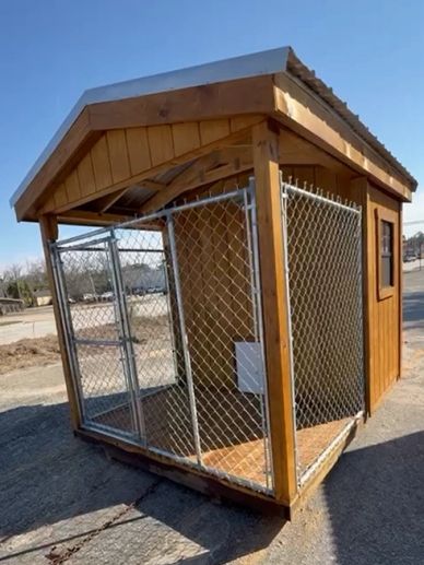 Wooden dog kennel with chain-link fenced area and metal roof.
