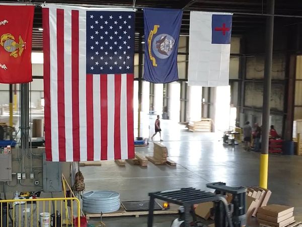 Flags of the US military branches and the American flag hang in a spacious warehouse.
