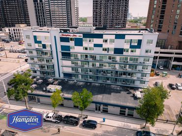 Hampton Inn by Hilton hotel building in downtown Winnipeg with parked cars and trees.
