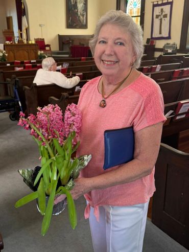 Smiling elderly woman holding pink flowers in a church.
