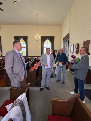 Four men conversing inside a church with stained glass windows.