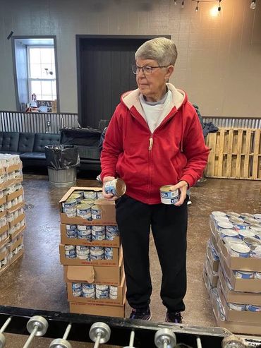 Elderly woman sorting canned goods in a warehouse.
