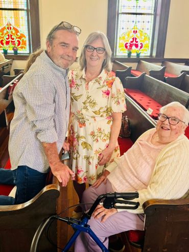 Three smiling adults inside a church with stained glass windows.