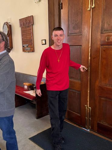 Young man in a red shirt opening a wooden door inside a church.