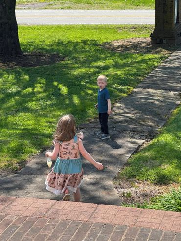 Two children play outside on a sunny day on a cracked sidewalk.
