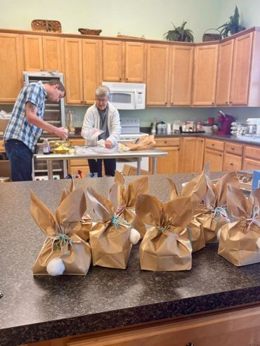 Two people packaging gifts in a kitchen with bunny-eared brown paper bags.