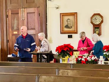 Four elderly people interacting in a room decorated with poinsettias and vintage clock.