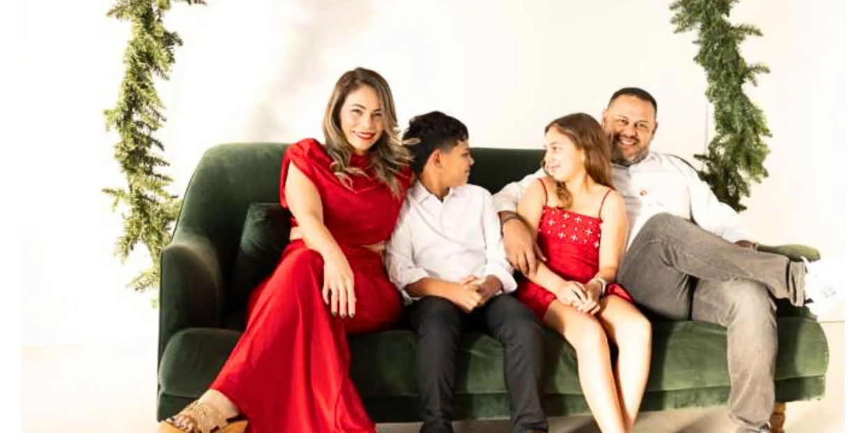 A family of four sitting on a green couch, dressed in festive red and white.