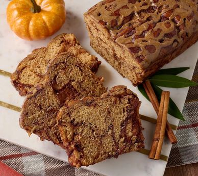 Sliced pumpkin bread with cinnamon sticks and a small pumpkin.