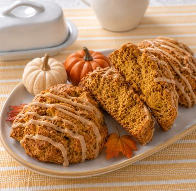 Pumpkin scones drizzled with icing, displayed with mini pumpkins and autumn leaves.