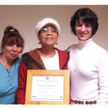 Three women smiling, one holding a framed certificate of appreciation.