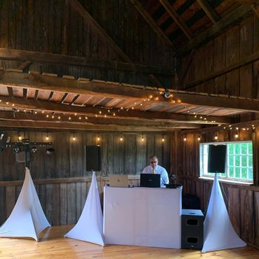 A DJ setup in a rustic wooden room with string lights and white speaker covers.