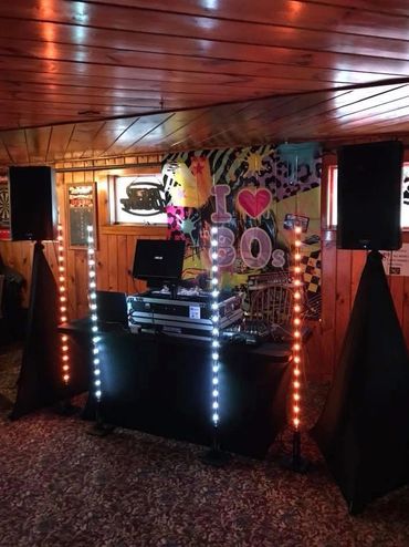 DJ setup with colorful lights and an 80s-themed backdrop in a wooden room.
