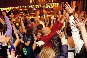 A lively crowd dancing with hands raised at an indoor event.