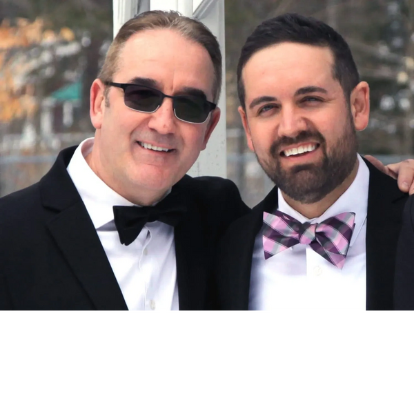 Two men in tuxedos smiling at the camera, one wearing sunglasses and the other a colorful bow tie.