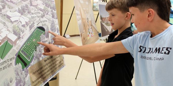 Two boys pointing at a stadium layout on a poster.