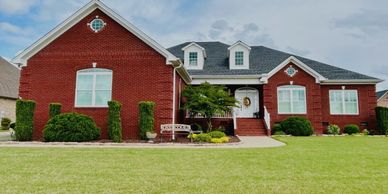 Large red brick house with a well-kept lawn and shrubs.