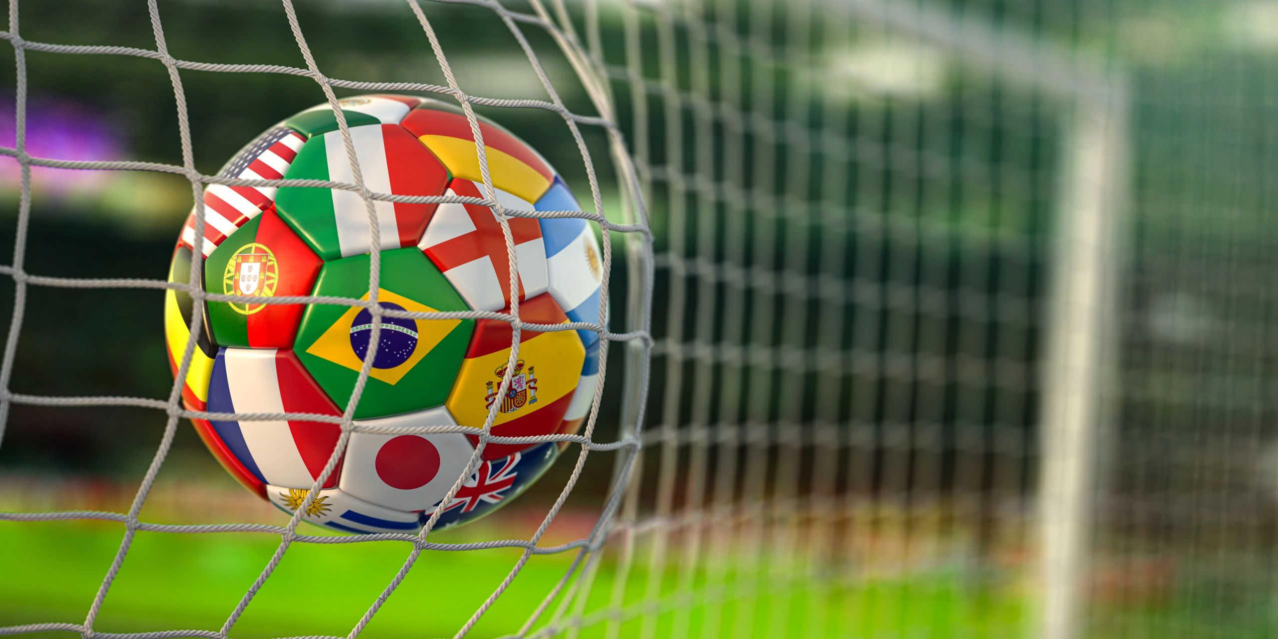 Soccer ball with international flags hits the goal net on a sunny field.