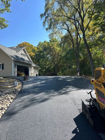 Freshly paved driveway in front of a house under clear blue sky.