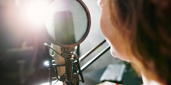 Person speaking into a microphone in a recording studio.