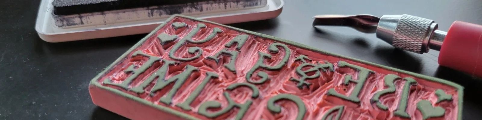 A hand carving tool sits next to a finished linocut stamp