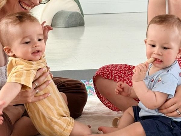 Two babies sitting on the floor with adults.