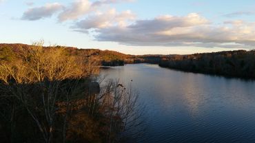 A calm river flowing between autumn-colored trees under a cloudy sky.
