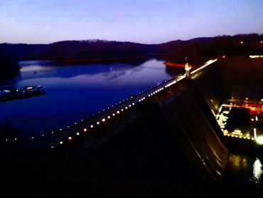 Evening view of a dam with lights reflecting on the water.