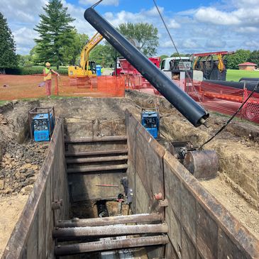 Construction site with large trench and pipe being lowered.
