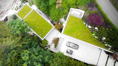 Aerial view of modern house with green roofs and cars parked on the driveway.